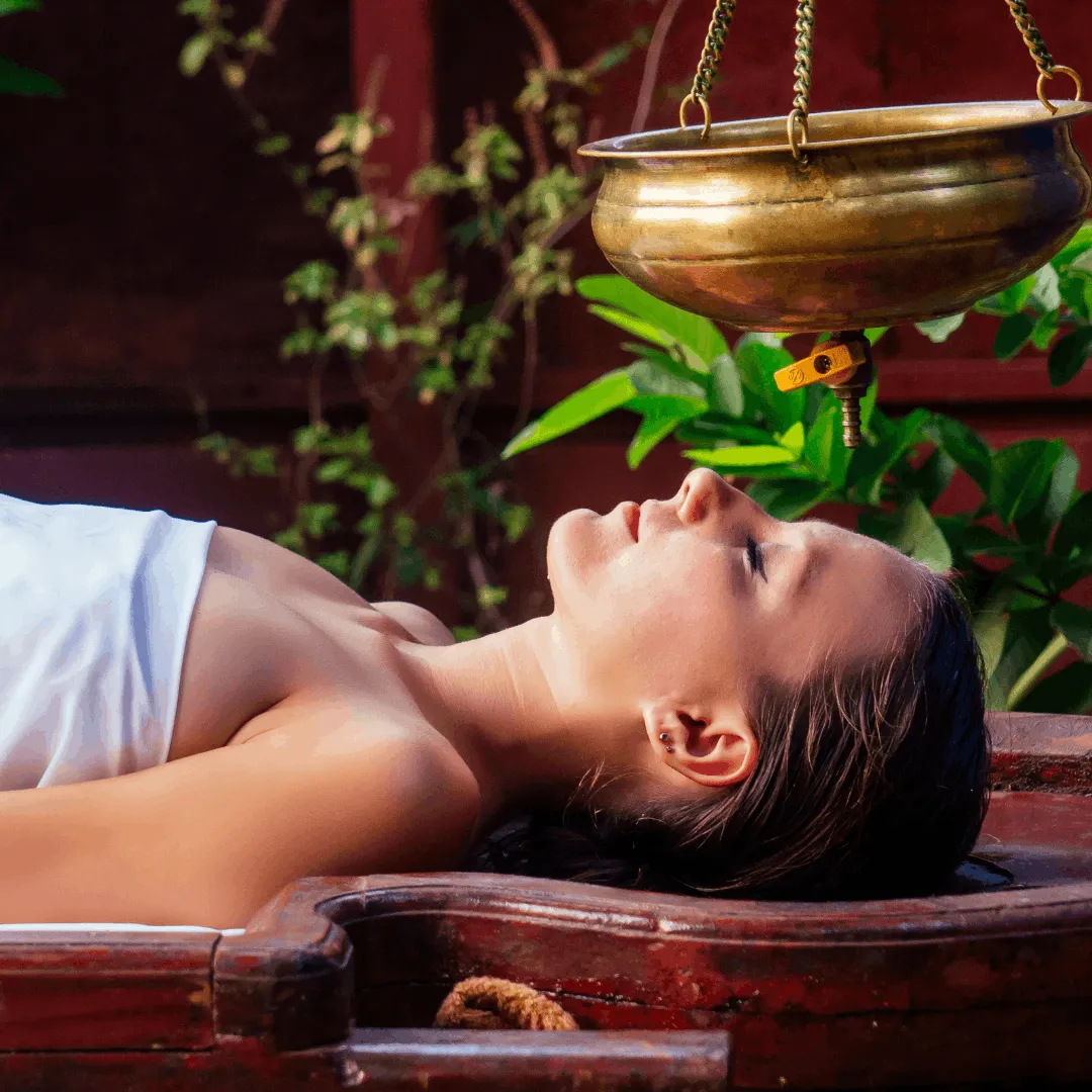 Warm medicated oil streaming from copper Shirodhara vessel onto patient forehead at Vedara Care Ayurveda clinic, JVC Dubai